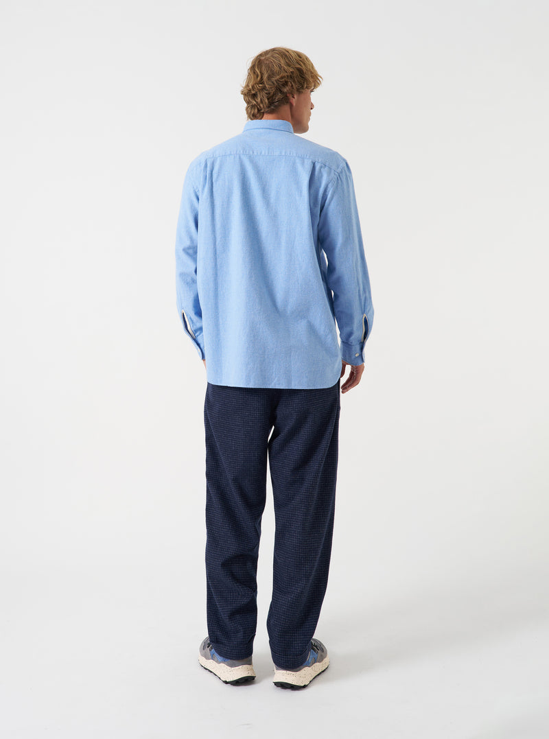 A male model poses against a neutral studio backdrop wearing the Blue Brushed Flannel Square Pocket Shirt. The angled view showcases the fit across the shoulders, sleeve construction, and soft flannel texture.