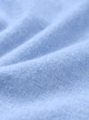 Close-up of the brushed flannel fabric used in the blue square pocket shirt. The tight knit weave is clearly visible, with a soft, lightly napped surface in a pale sky blue. Gentle folds show the fabric's drape and texture across the full frame.