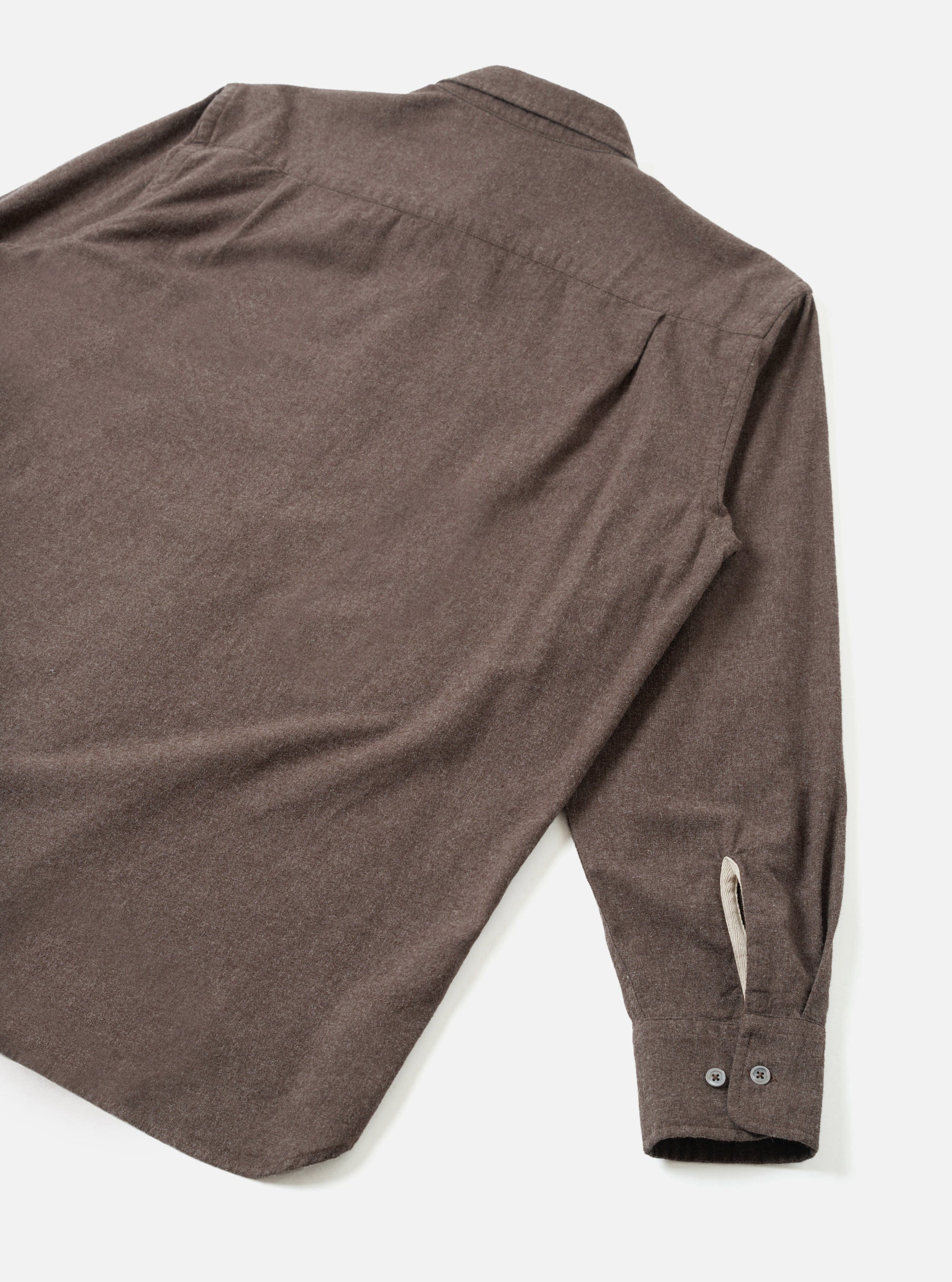 Flat lay of a brown brushed flannel shirt on a white surface, shot from behind at an angle. The back yoke and one long sleeve are visible, ending in a buttoned cuff with two dark buttons and a cream contrast placket. The fabric has a soft, matte flannel texture in a heathered brown tone.