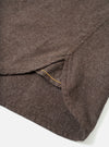 Close-up detail of a brown brushed flannel shirt laid flat on a white surface. The shot focuses on the curved shirt hem and a side seam vent, with a yellow contrast stitch visible along the vent opening. A small button is visible at the upper right. The fabric shows a soft, mélange flannel texture.