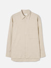 Ecru brushed flannel long-sleeve shirt laid flat on a light grey studio backdrop. Features a point collar, full button placket with tonal buttons, a single patch chest pocket on the left, buttoned cuffs, and a curved shirttail hem. The fabric has a soft, lightly textured flannel weave. A Universal Works woven label sits at the back collar.
