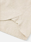 Close-up of the hem and side seam area of an ecru brushed flannel shirt, shot on a white studio surface. The soft, lightly textured flannel fabric is visible in detail. A side vent opening is shown at the hem, with a single yellow accent stitch visible at its base.