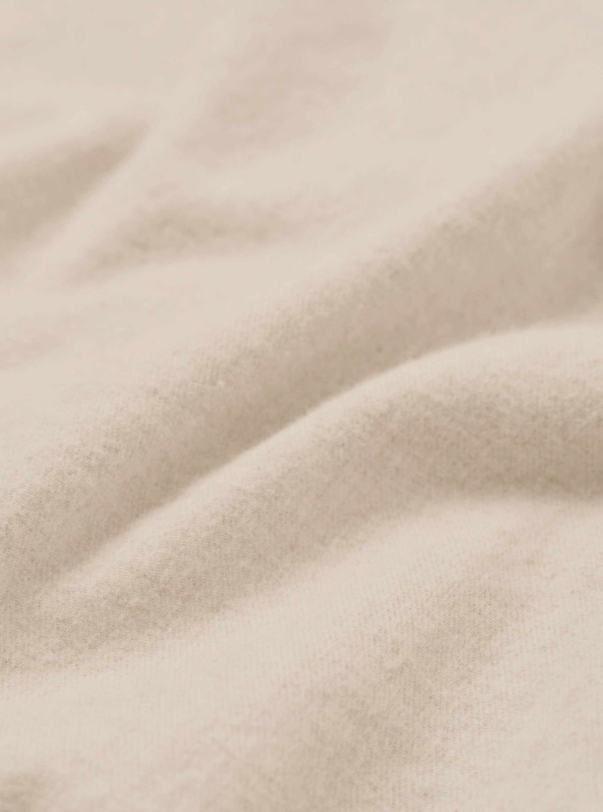 Close-up of the ecru brushed flannel fabric, showing soft, lightly napped texture with gentle folds and a warm off-white tone. Fine knit fibres are visible across the surface. No garment details or background are visible in this detail shot.