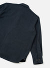 Flat lay of a navy flannel overshirt on a white surface, shot from above at an angle showing the back and right sleeve. The textured twill-weave flannel fabric has a subtle melange finish. A seam runs vertically down the back. The cuff is fastened with two dark horn-effect buttons. The curved shirt-tail hem is visible at the bottom corner.