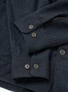 Close-up flat lay of a navy flannel overshirt on a white surface, focusing on the cuffs and front placket. The fabric has a textured twill weave with subtle tonal stripe. Four-hole horn-effect buttons fasten the barrel cuffs and placket. Two overlapping sleeves show double-button cuffs in detail.