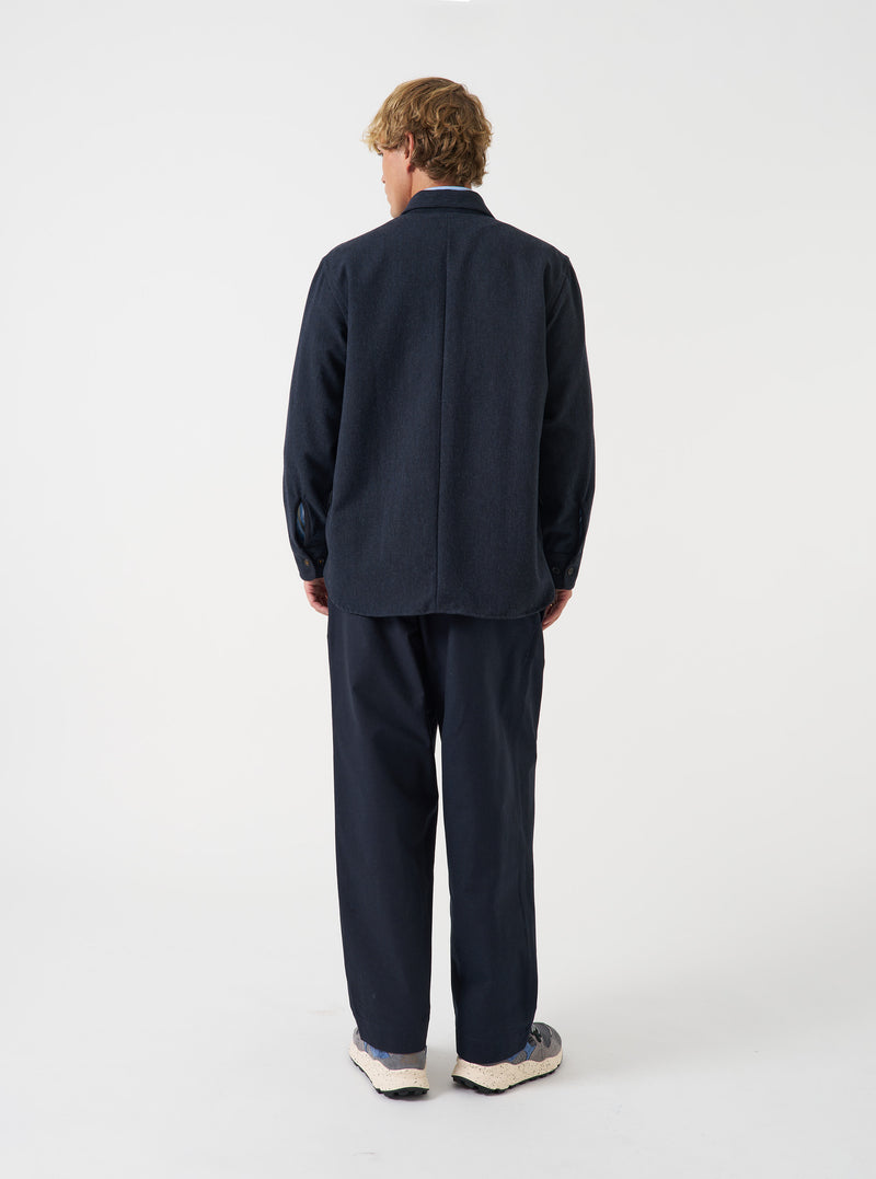 A male model wears the Navy Airline Flannel Travail Overshirt unbuttoned in a side-angled pose against a neutral background. The shot displays the relaxed layering fit, structured collar, and deep navy hue.