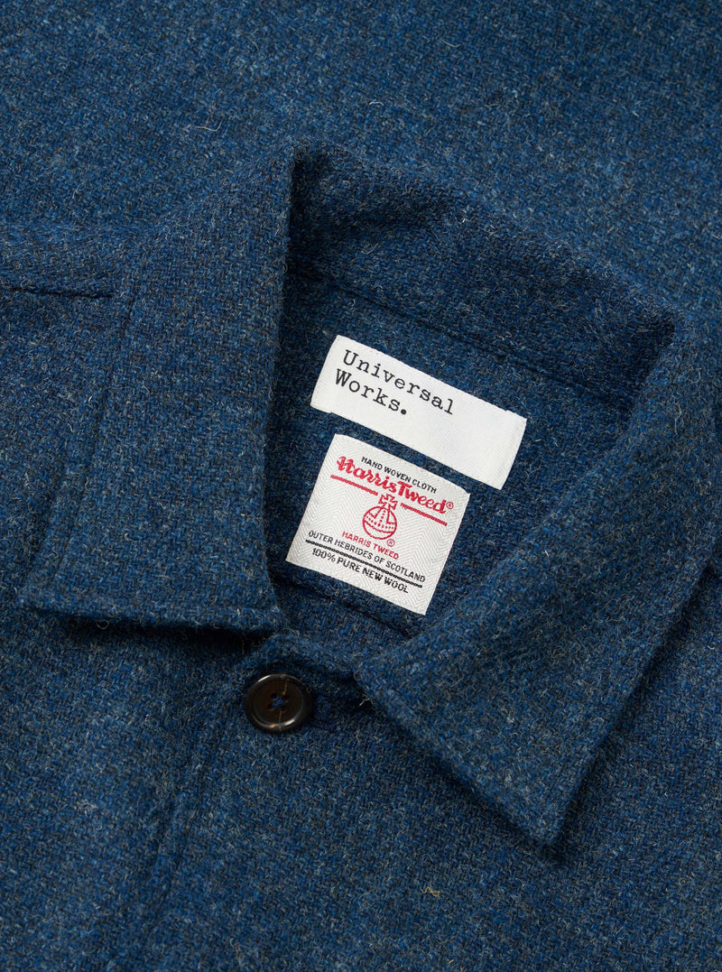 A close-up detail shot of the Blue Harris Tweed Easy Jacket placed on a plain background. The angled view emphasizes the front buttoning, pocket construction, lapel edge, and wool fabric weave.