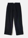 Flat lay of black corduroy wide-leg chinos on a white studio backdrop. The ribbed cord texture is visible across the full length. Features a single button fly, front pleats, slant side pockets, belt loops, and a straight wide hem. A small branded label sits at the inner waistband.