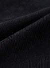 Close-up detail shot of black corduroy fabric showing wide-wale cord texture. The parallel ridges and soft pile of the material are clearly visible across the draped folds of the Black Cat Cord Grad Chino. No background is visible.