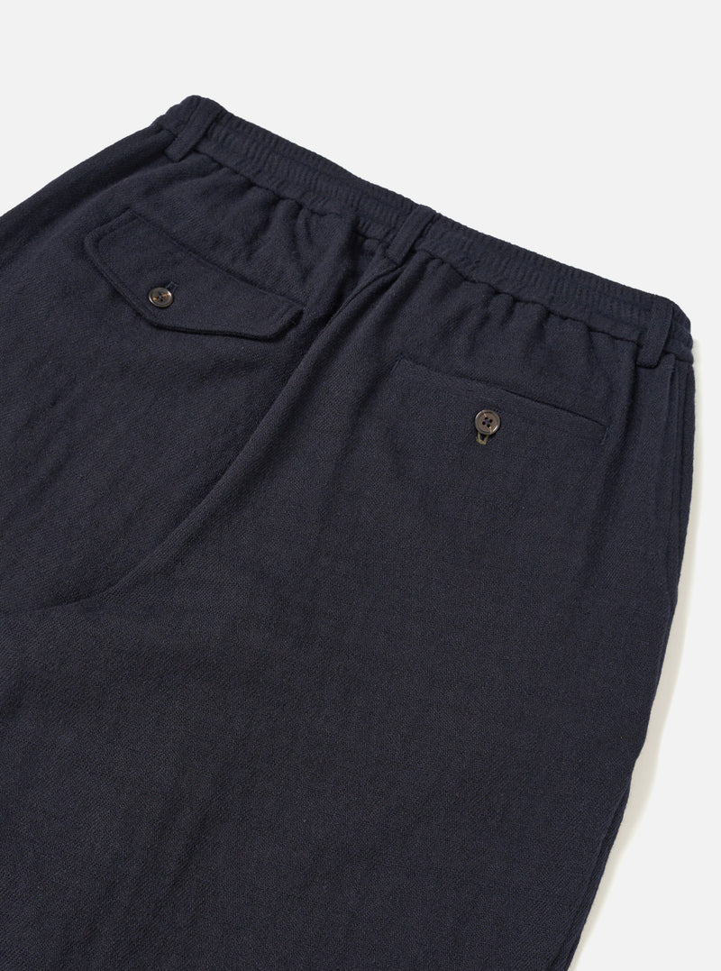 A male model wears the Dark Navy Robin Wool Mix Pleated Track Pant with a casual top, standing against a neutral studio backdrop. The full-length shot shows the tapered leg and loose fit.