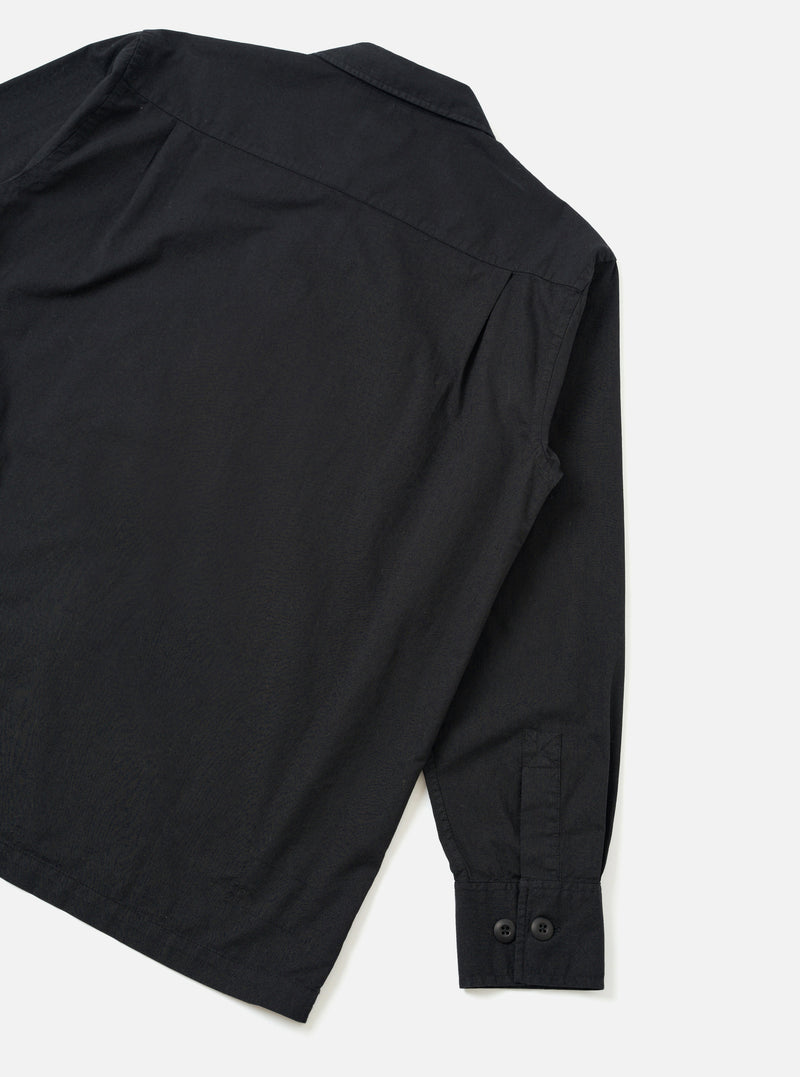 Rear view of the Black Slub Shirting Fatigue Shirt presented on a solid off-white background. The shot highlights the smooth back panel, clean hemline, straight shoulder seams, and slub texture of the cotton fabric.