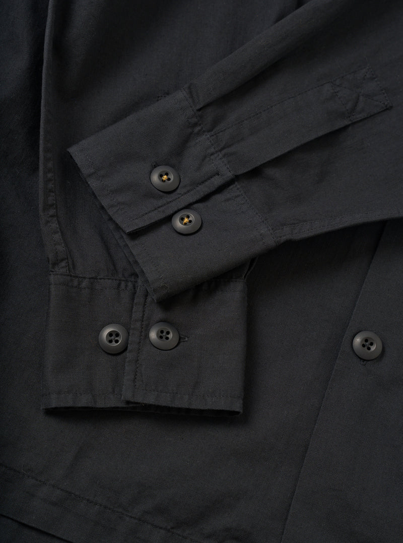 A detailed close-up shot of the Black Slub Shirting Fatigue Shirt set against a plain background. The view emphasizes the textured slub cotton fabric, neat chest pocket stitching, and front button closure details.