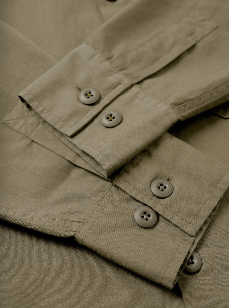 A close-up detail shot of the Olive Slub Shirting Fatigue Shirt against a plain background, highlighting the rich slub texture of the cotton fabric alongside fine stitching around the button closures and chest pocket.