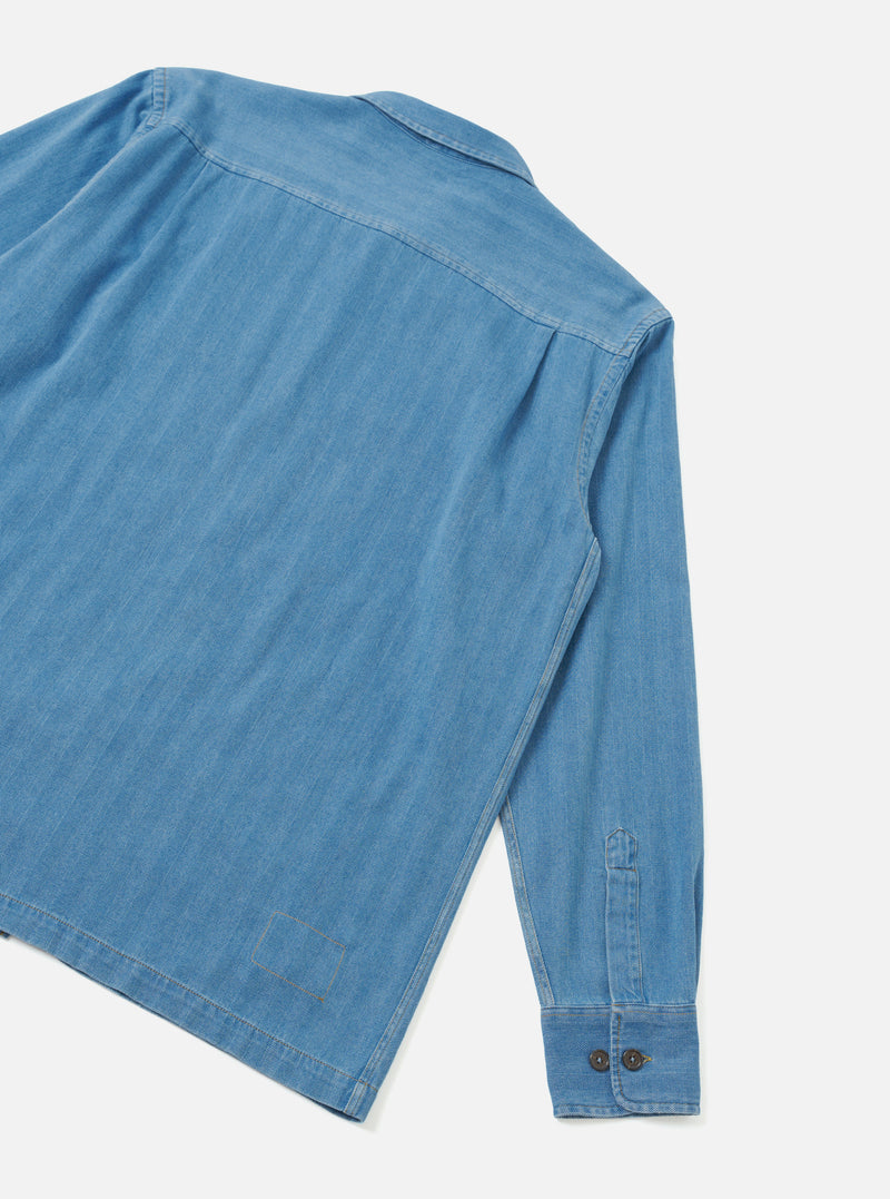 Back view of the Washed Indigo Recycled Herringbone Attendant Shirt displayed on an off-white background. The shot highlights the clean rear hem, back yoke, shoulder construction, and subtle herringbone weave.