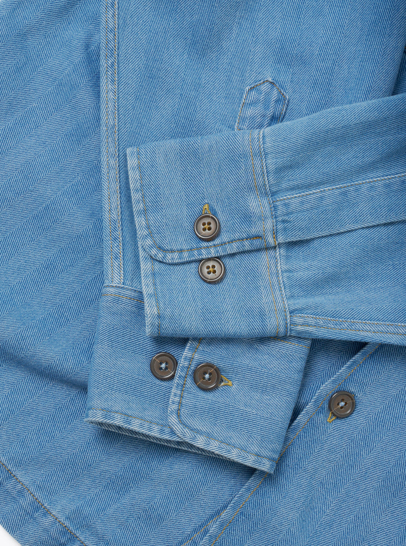 Close-up detail image of the Washed Indigo Recycled Herringbone Attendant Shirt on a plain background, focusing on the textured recycled cotton herringbone pattern, durable stitching, and button placement.