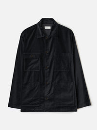 Black velvet chore jacket laid flat on a white studio backdrop. Spread collar with a Universal Works woven label at the neckline. Five dark buttons down the centre front placket. Two flap chest pockets and two large open patch pockets at the lower front. Long sleeves with plain cuffs. Straight hem.