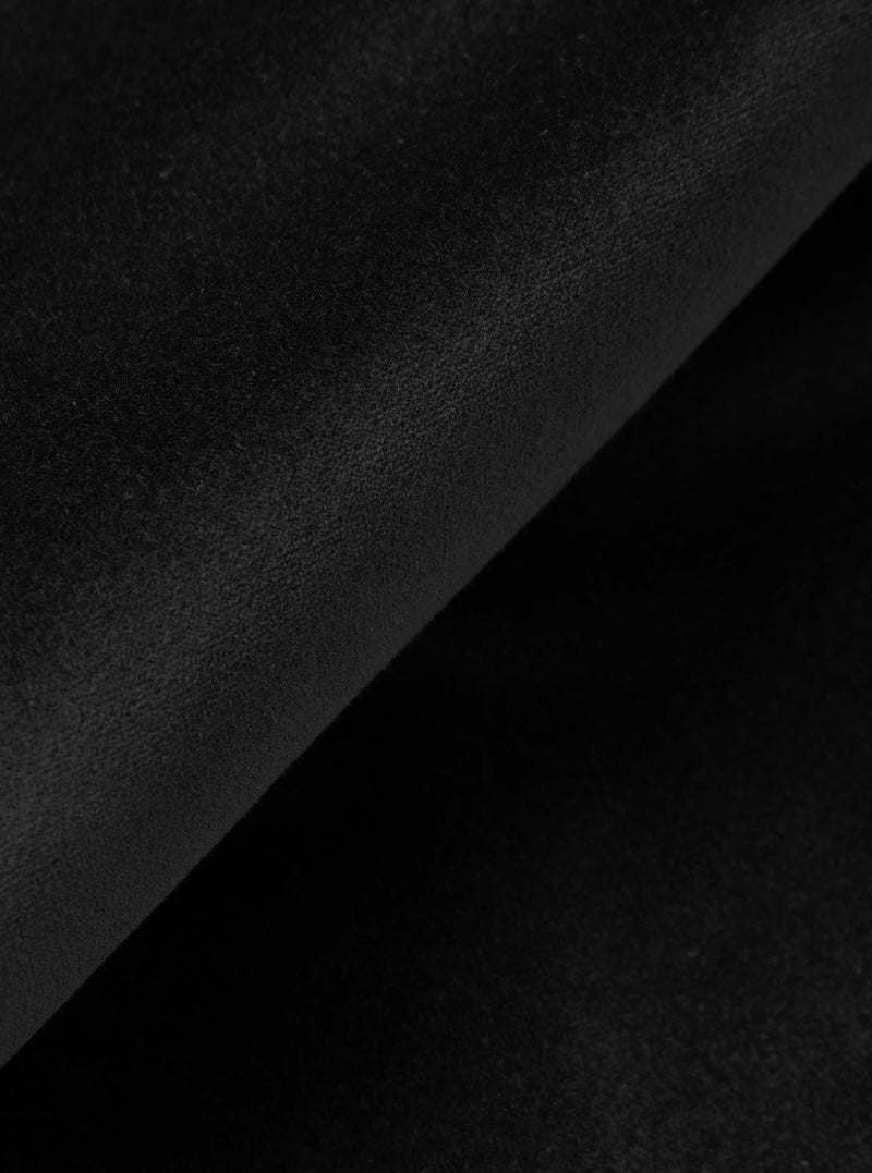Close-up detail shot of black velvet fabric, showing a diagonal fold across the frame. The matte, fine-pile surface catches subtle light variation, revealing the texture and depth of the material against the darker shadow of the fold beneath.