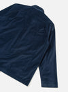Navy velvet overshirt laid flat on a light grey seamless backdrop, shot from above at an angle. The back and right sleeve are visible, showing the yoke seam, a folded cuff, and the straight hem. The fine-pile velvet fabric catches the light, showing subtle sheen across the body.