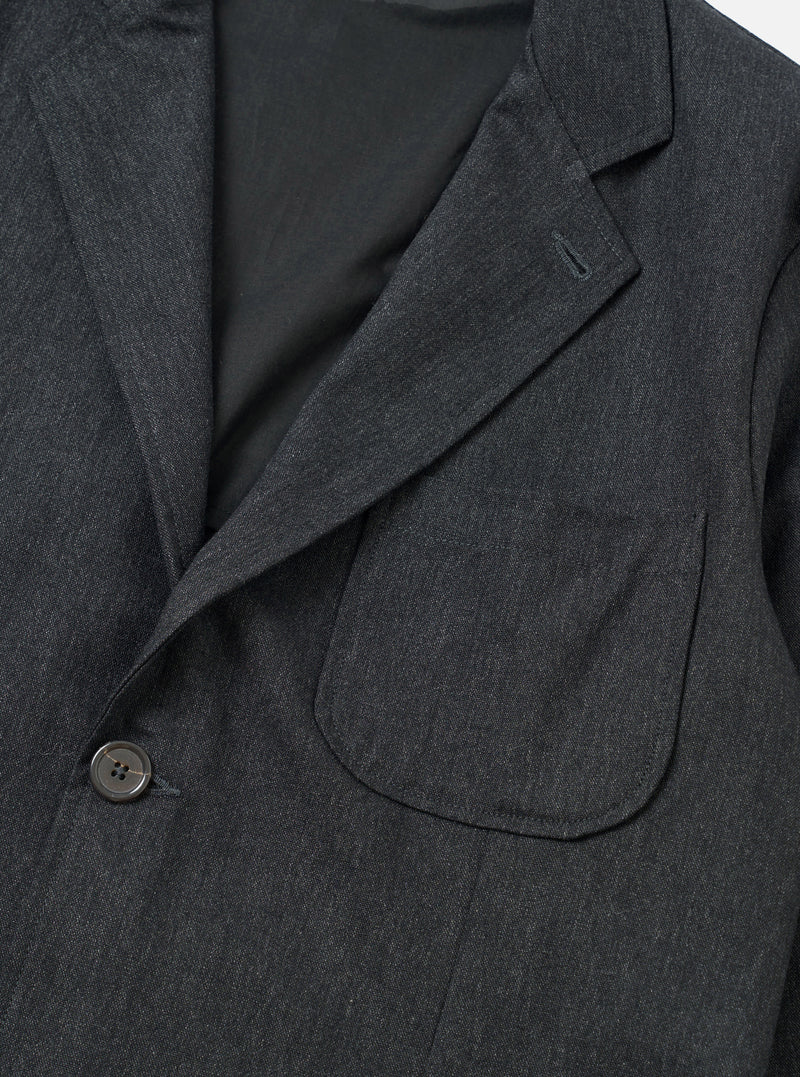 An angled view of the Charcoal Recycled Italian Tweed Two Button Jacket displayed against a simple light background. The shot emphasizes the soft collar line, front patch pockets, and tactile recycled wool blend material.