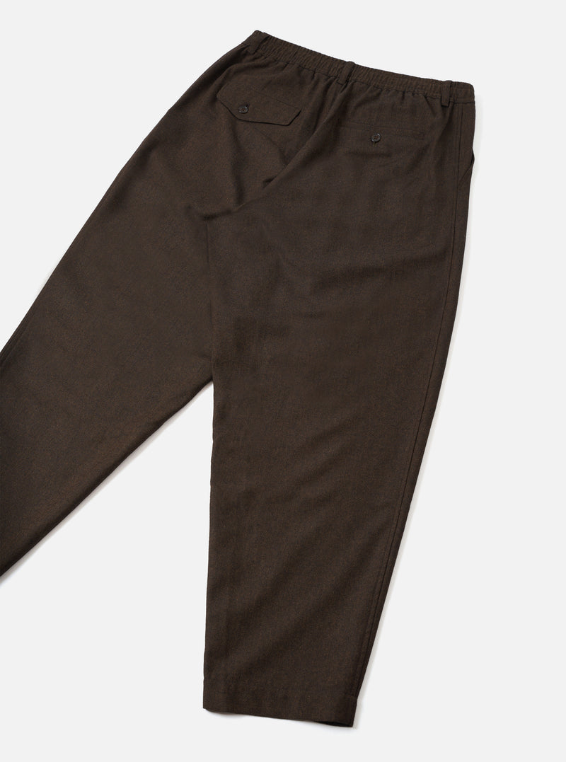 A back view of a model wearing the Brown Recycled Italian Tweed Pleated Track Pant against a plain studio background. The shot highlights the relaxed fit, rear pockets, and textured brown tweed material.