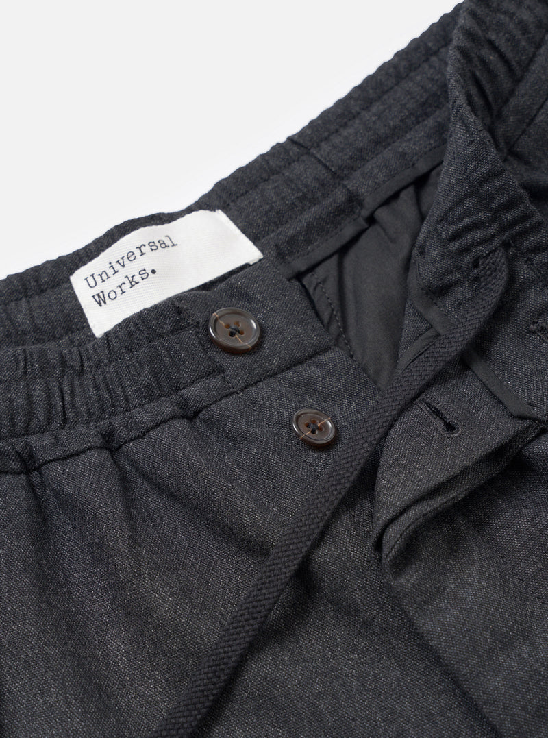 A close-up view of a model wearing the Charcoal Recycled Italian Tweed Pleated Track Pant, highlighting the pleated front, waistband, and drawstring detail against a plain background.