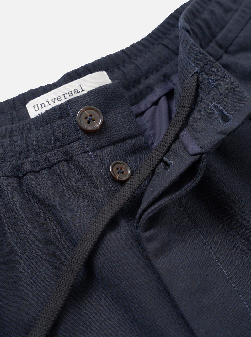 A close-up view of a model wearing the Navy Recycled Italian Tweed Pleated Track Pant against a plain studio background, focusing on the pleats, waistband construction, and textured navy wool blend fabric of the trousers.