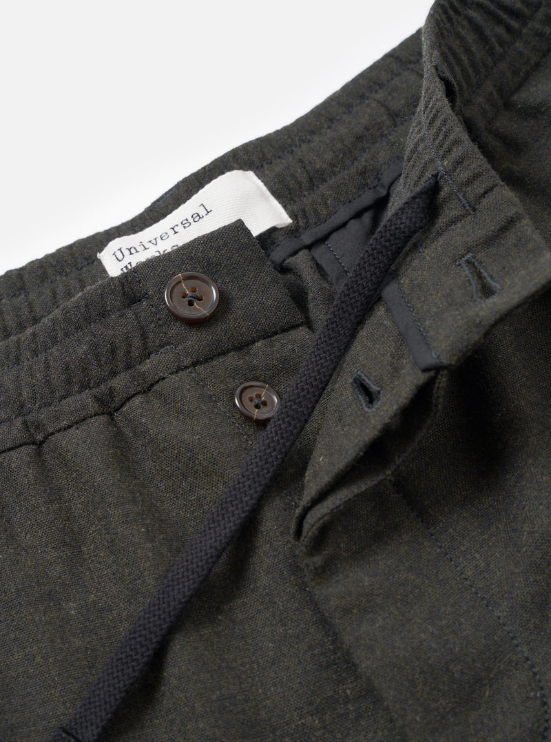 A close-up shot of a model wearing the Olive Recycled Italian Tweed Pleated Track Pant, focusing on the front waistband, pleat construction, and drawstring detail against a clean studio backdrop.