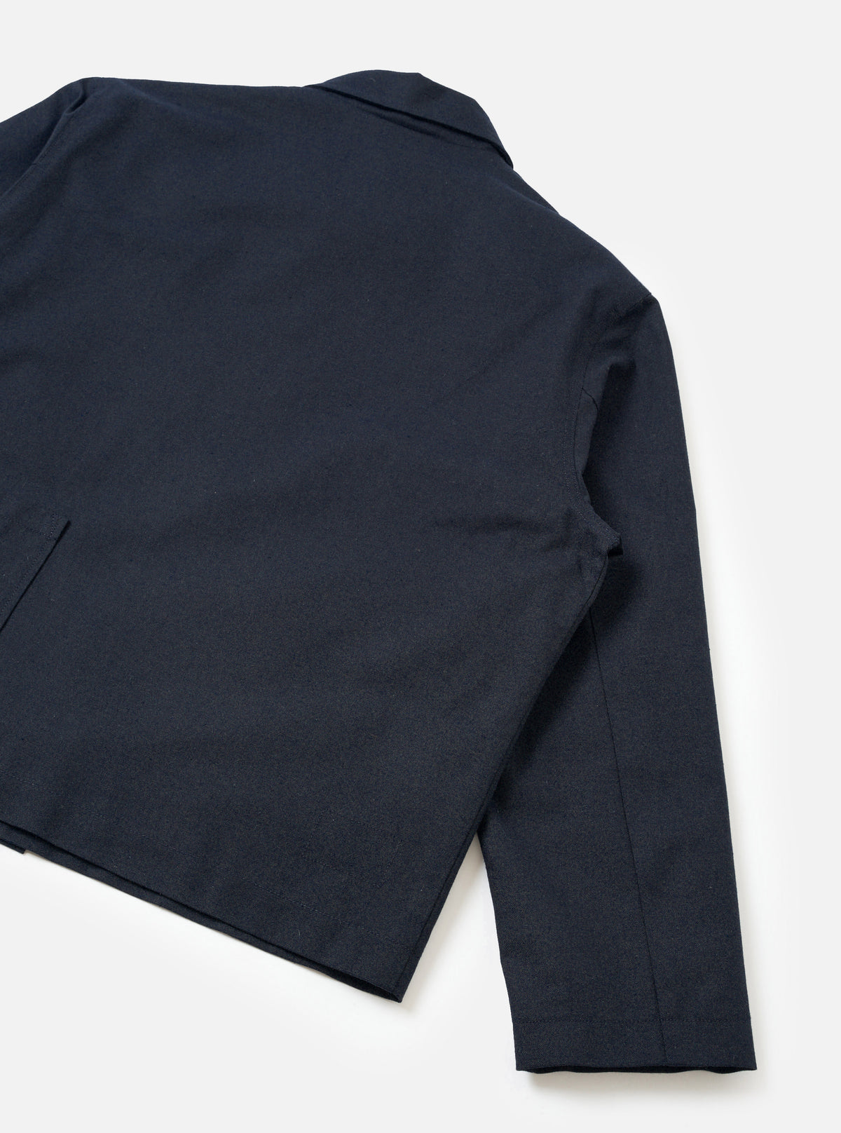 A back view of a model wearing the Navy Lucca Suiting Ives Jacket against a simple studio background, highlighting the straight hem, comfortable tailoring, and clean finish of the navy blue cotton blend fabric.