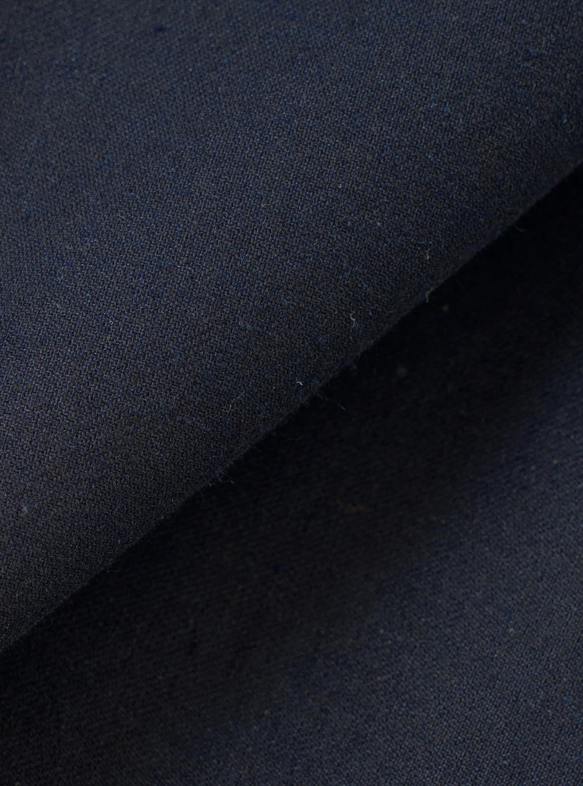 A detailed close-up fabric swatch photograph of the Navy Lucca Suiting Ives Jacket set against a plain white background, revealing the subtle weave pattern and fine texture of the navy cotton and acrylic fabric.