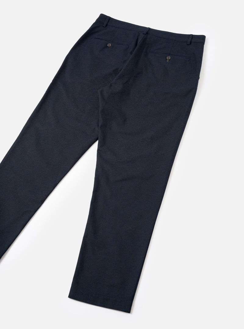 A rear view of a model wearing the Navy Lucca Suiting Military Chino in a studio setting, showing the back pocket placement, waist construction, and tailored straight leg silhouette of the navy blue trousers.