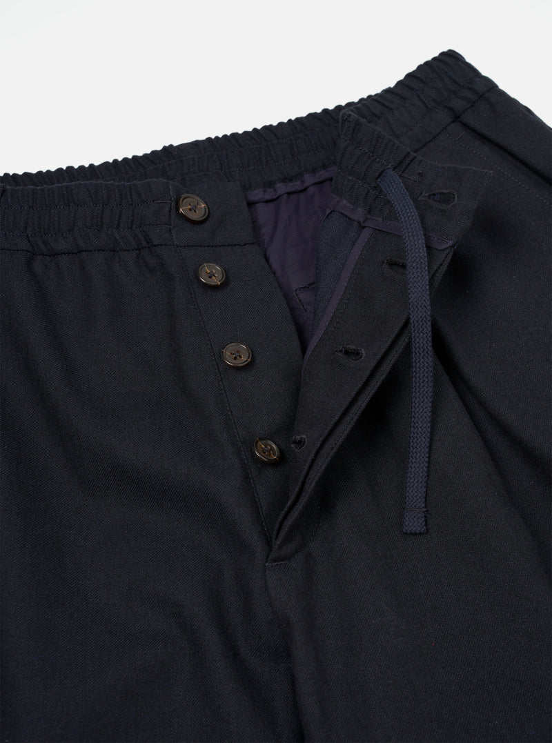 A detailed close-up shot of the Navy Lucca Suiting Oxford Pant on a plain white background, highlighting the waistband with adjustable drawstring, button fly, front pleating, and subtle fabric texture.
