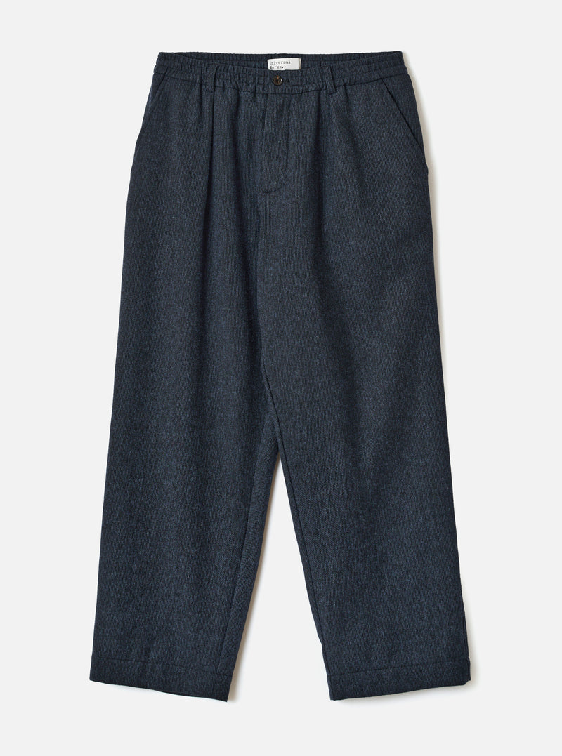 Navy flannel Oxford trousers laid flat on a light grey studio backdrop. The fabric has a fine pinstripe texture in navy. Features an elasticated waistband with a single button closure, a woven brand label, front pleats, slanted side pockets, and turned-up cuffs at the hem. Wide, relaxed leg with a tapered ankle.
