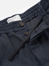 Close-up of the waistband detail on the Universal Works navy flannel Oxford pant. A wide elasticated waistband sits above a button fly with two dark horn-style buttons and a woven drawcord. A white branded label is visible inside. The twill-weave flannel fabric shows a navy and dark grey marl texture. Plain white studio backdrop.