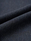 Close-up fabric detail of the navy airline flannel oxford pant, showing a charcoal and navy twill-weave wool flannel with a fine diagonal rib texture and visible surface fibres. The fabric is folded to reveal depth and drape, shot against a matching dark flannel background.