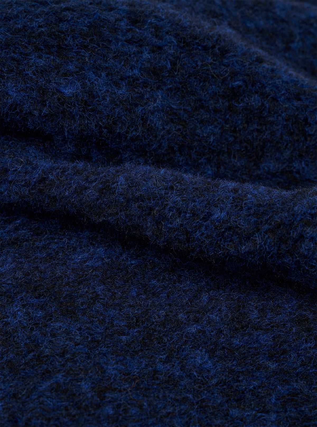 Close-up of the navy blue boucle style fleece fabric of the Lancaster Jacket, showing a looped, textured weave with visible fibre strands in deep blue and dark tones. The fabric is folded to highlight its soft, fluffy surface and dimensional texture.