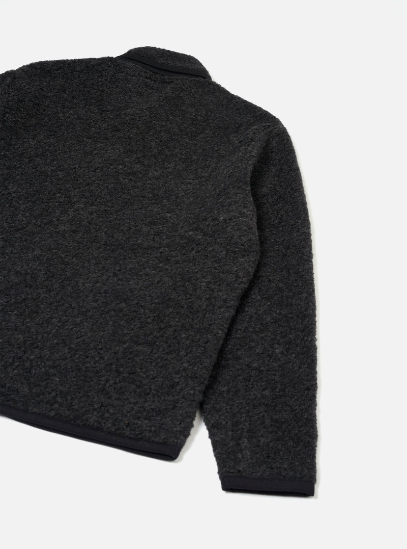 Charcoal boucle style fleece Lancaster jacket shot flat on a plain light grey backdrop. The rear three-quarter view shows the textured boucle style fabric across the back and one sleeve, with contrast black ribbed trim at the cuff and hem. A black collar is visible at the top neckline.