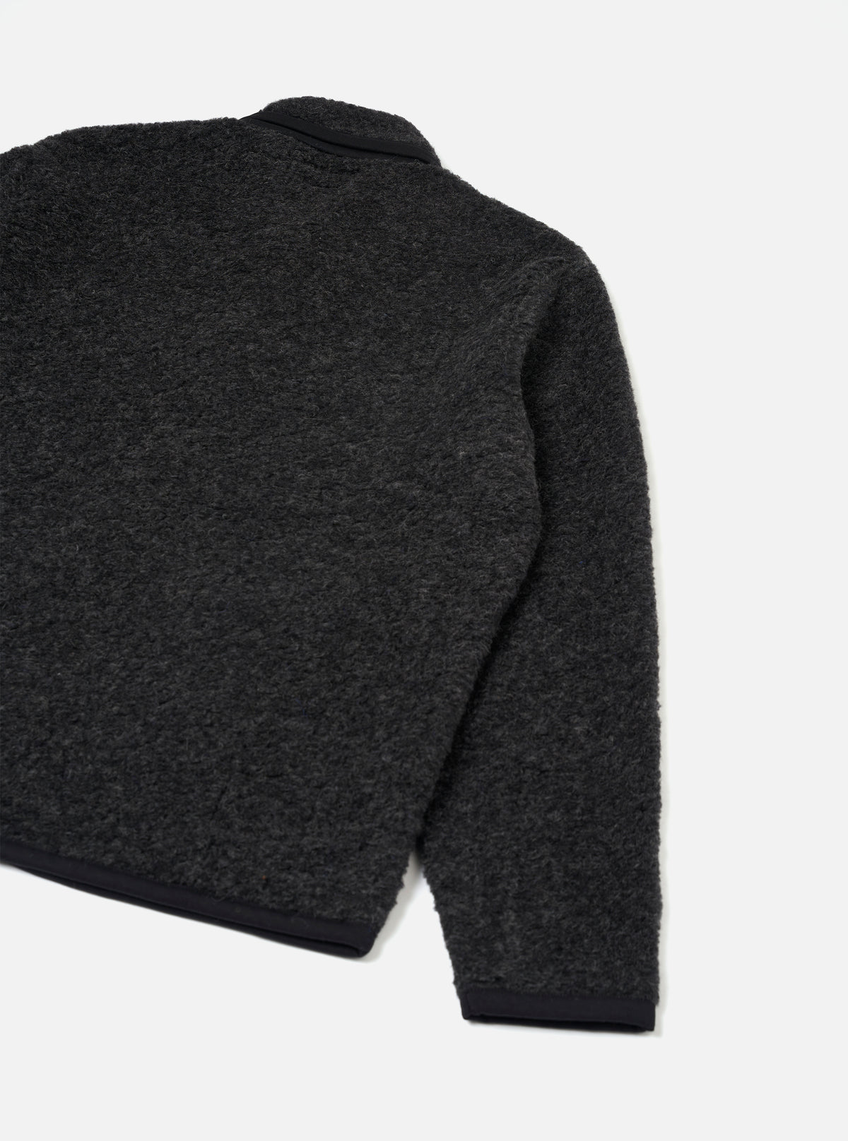 Charcoal boucle style fleece Lancaster jacket shot flat on a plain light grey backdrop. The rear three-quarter view shows the textured boucle style fabric across the back and one sleeve, with contrast black ribbed trim at the cuff and hem. A black collar is visible at the top neckline.
