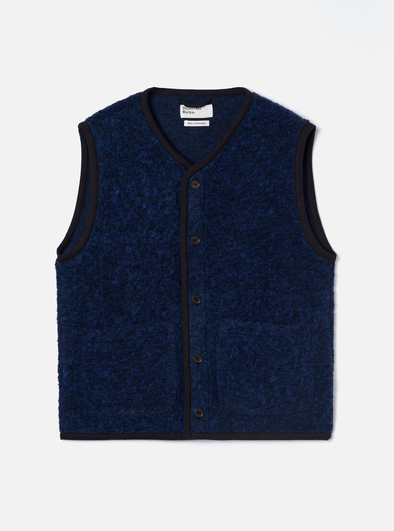 Blue boucle style fleece gilet laid flat on a light grey studio backdrop. V-neckline with dark navy binding trim running around the neck, armholes, front placket and hem. Five dark horn-effect buttons down the centre front. Two patch pockets at the lower front. Textured blue and black marl boucle style fabric throughout. Universal Works label visible at the neckline.