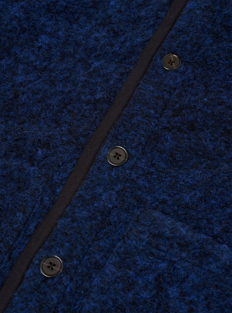 Close-up of the blue boucle style fleece Lancaster gilet, showing three dark four-hole buttons fastened along a navy grosgrain placket. The textured boucle style fabric has a looped, flecked surface in cobalt and dark navy tones. No model or mannequin is present.