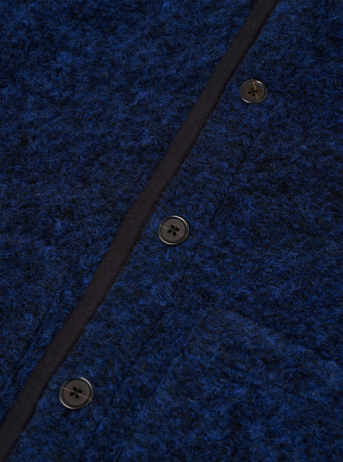 Close-up of the blue boucle style fleece Lancaster gilet, showing three dark four-hole buttons fastened along a navy grosgrain placket. The textured boucle style fabric has a looped, flecked surface in cobalt and dark navy tones. No model or mannequin is present.