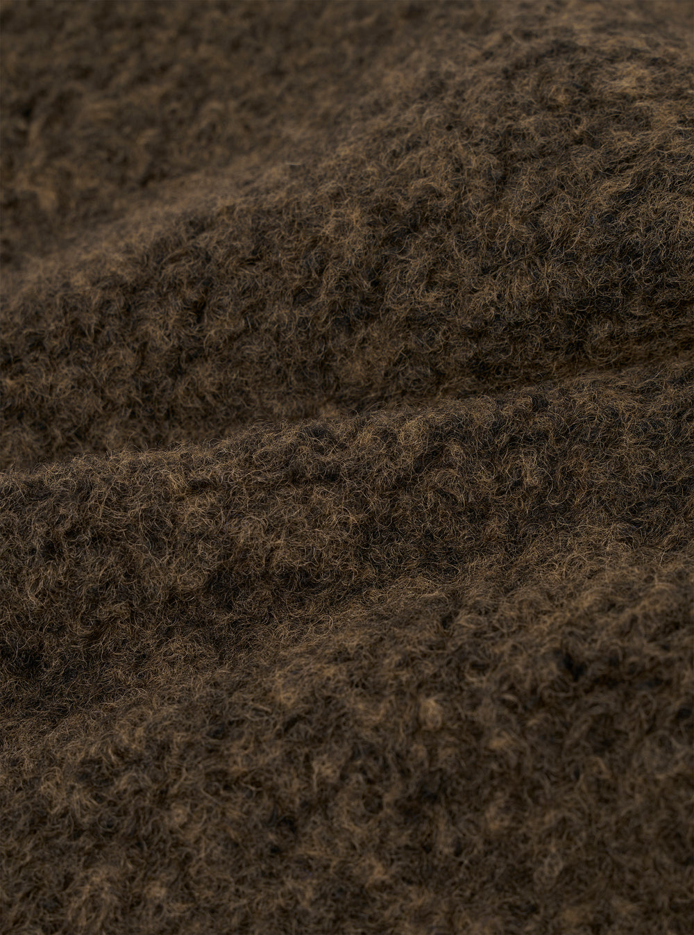 Close-up detail shot of the brown boucle style fleece fabric used in the Lancaster Gilet. The tightly looped, curly texture is clearly visible, with dark brown and warm tan tones running through the fibres. The image shows the fabric folded, highlighting its depth and soft, fluffy surface.