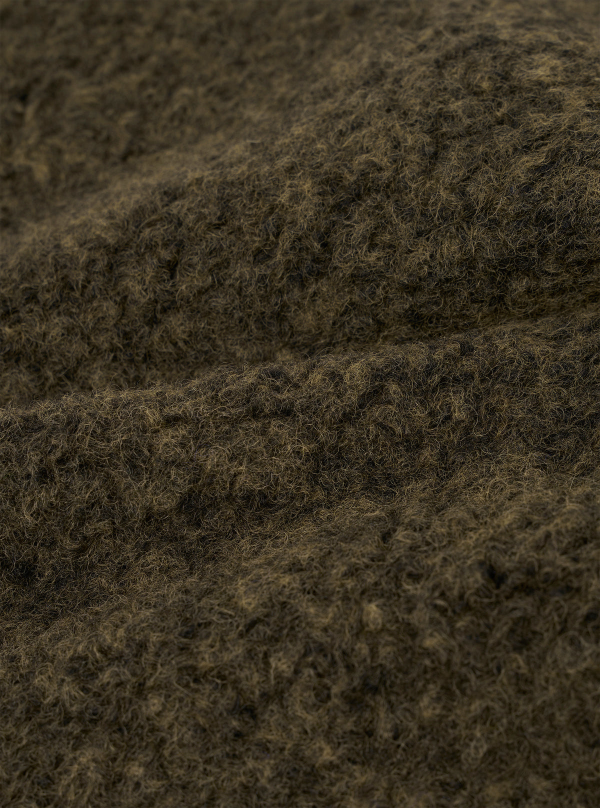 Close-up detail shot of the brown boucle style fleece fabric used in the Lancaster Gilet. The tightly looped, curly texture is clearly visible, with dark brown and warm tan tones running through the fibres. The image shows the fabric folded, highlighting its depth and soft, fluffy surface.