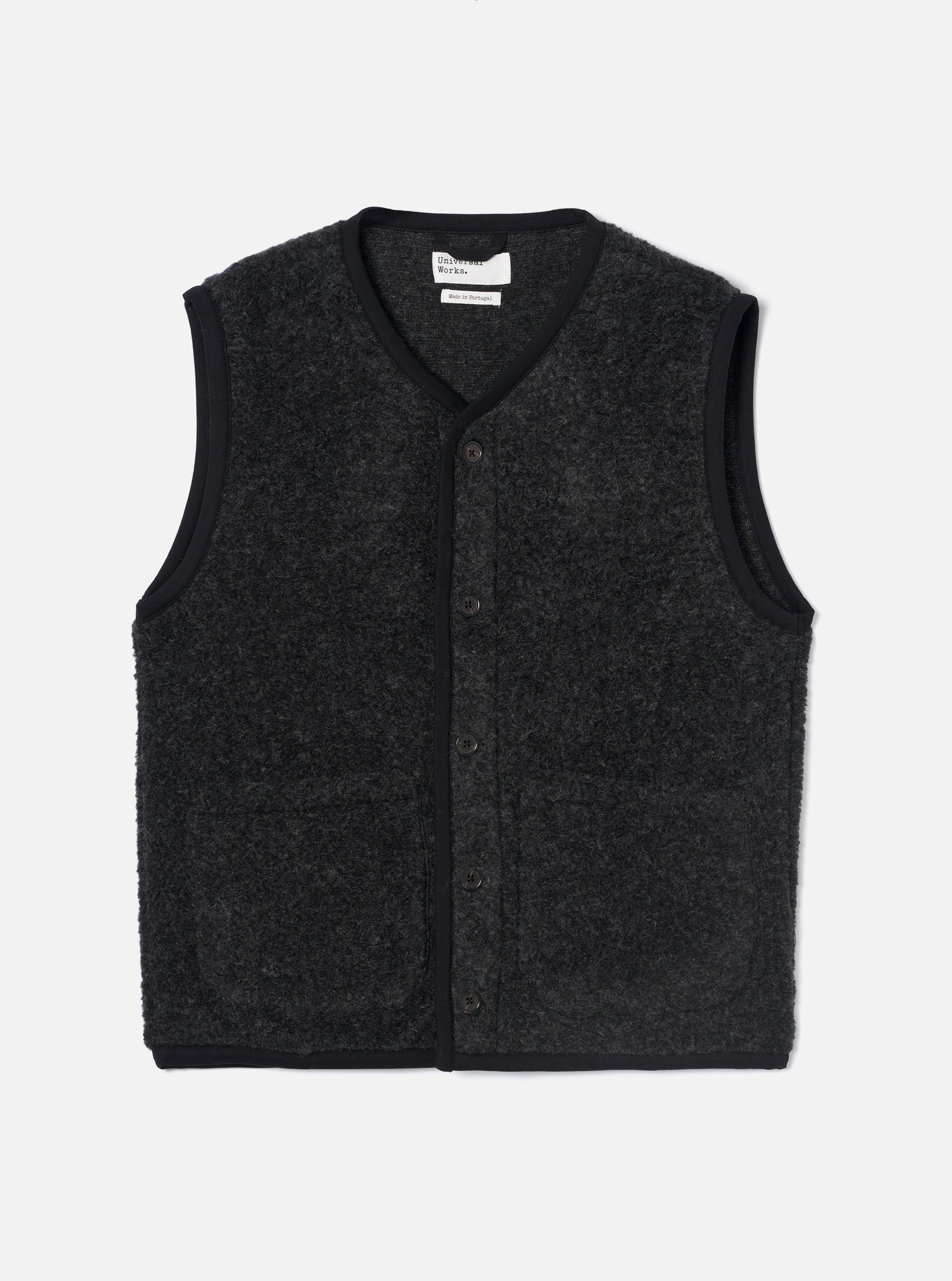 Charcoal boucle style fleece gilet laid flat on a light grey studio backdrop. V-neckline and armhole edges finished with black ribbed binding. Five dark buttons run down the centre front. Two patch pockets sit at the hem. A Universal Works woven label is visible at the inner neck.