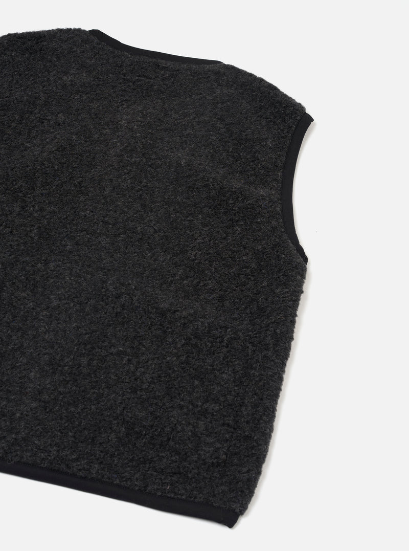 Charcoal boucle style fleece gilet laid flat on a white studio surface, shot at an angle showing the back and one armhole. The textured, looped fleece body is charcoal grey with contrast black binding along the armhole edge, neckline and hem.