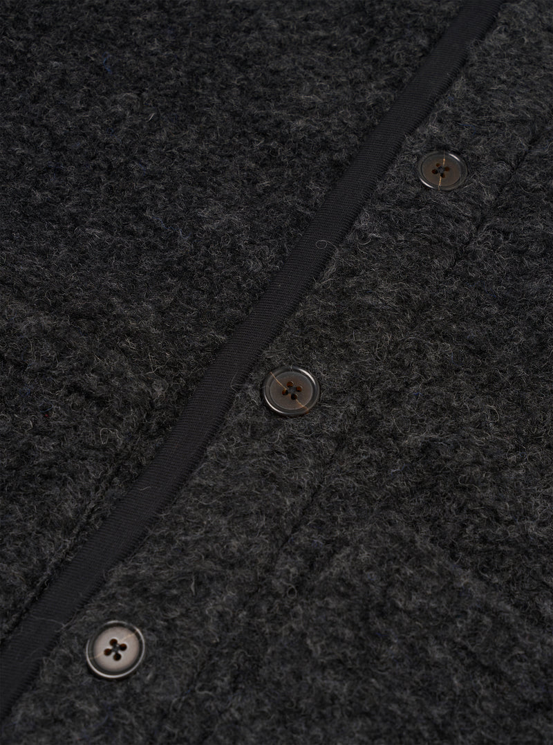 Close-up detail of the charcoal boucle style fleece gilet, showing the button placket with three four-hole horn-effect buttons and a narrow black grosgrain trim edging the front opening. The boucle style texture is clearly visible across the body of the gilet.