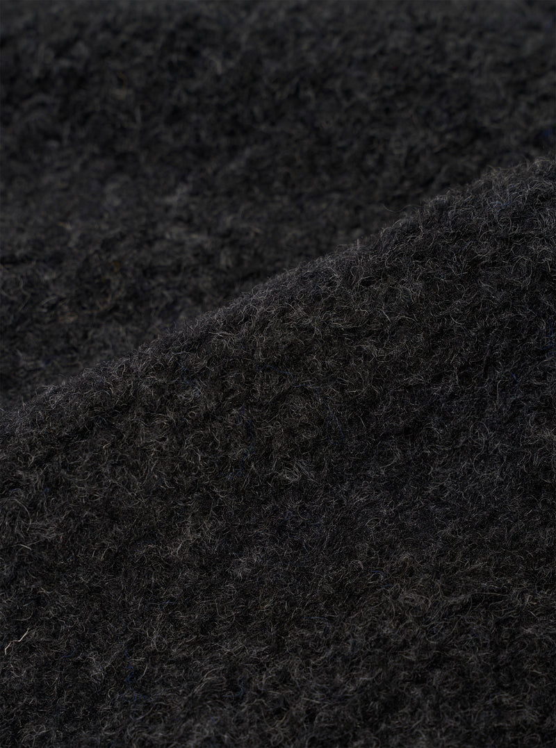 Close-up detail shot of the charcoal boucle style fleece fabric used in the Lancaster Gilet. The curly, looped texture of the boucle style fabric is clearly visible, showing tightly coiled fibres in a dark charcoal grey tone with subtle variations in depth across the surface.