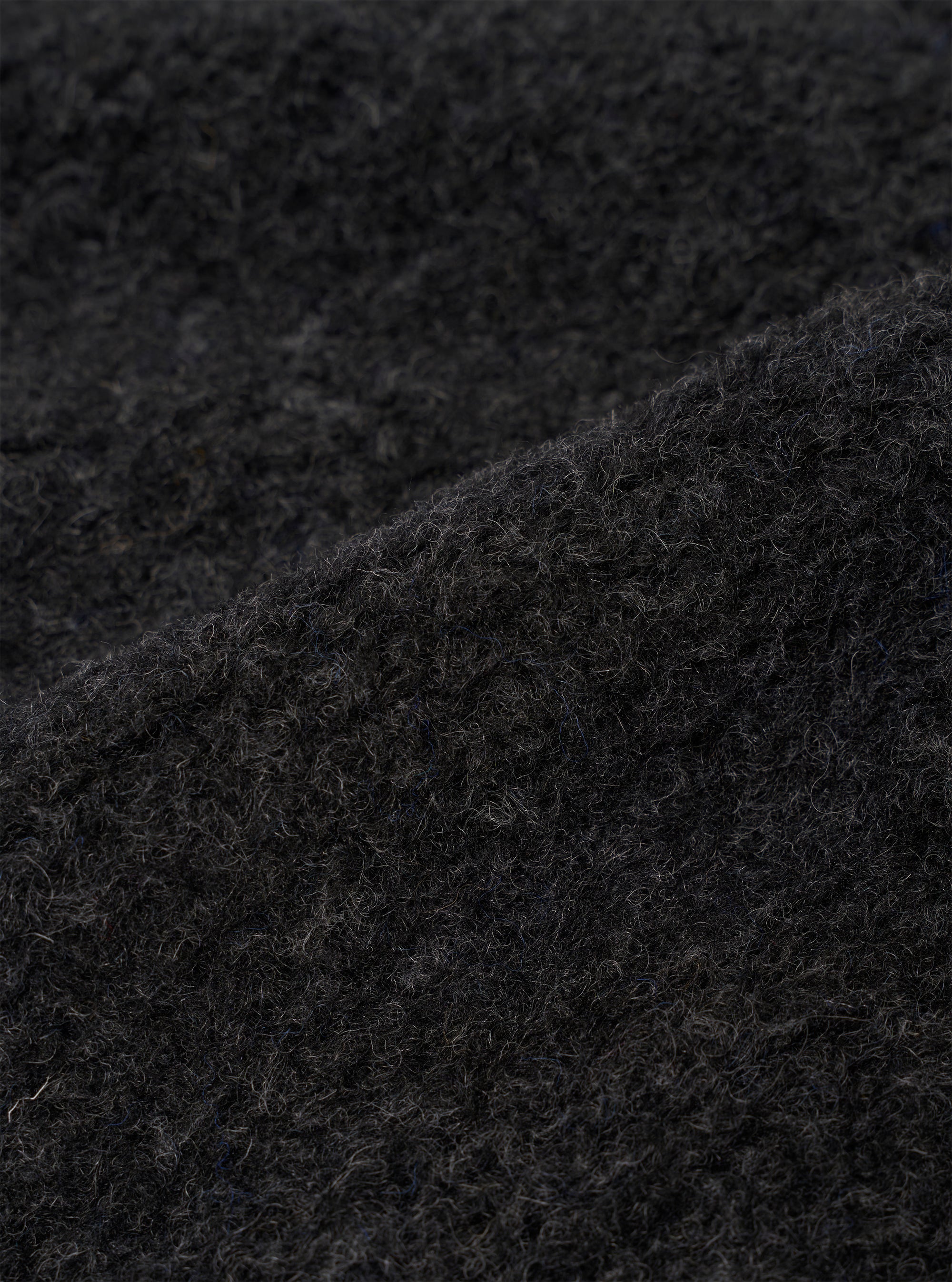 Close-up detail shot of the charcoal boucle style fleece fabric used in the Lancaster Gilet. The curly, looped texture of the boucle style fabric is clearly visible, showing tightly coiled fibres in a dark charcoal grey tone with subtle variations in depth across the surface.