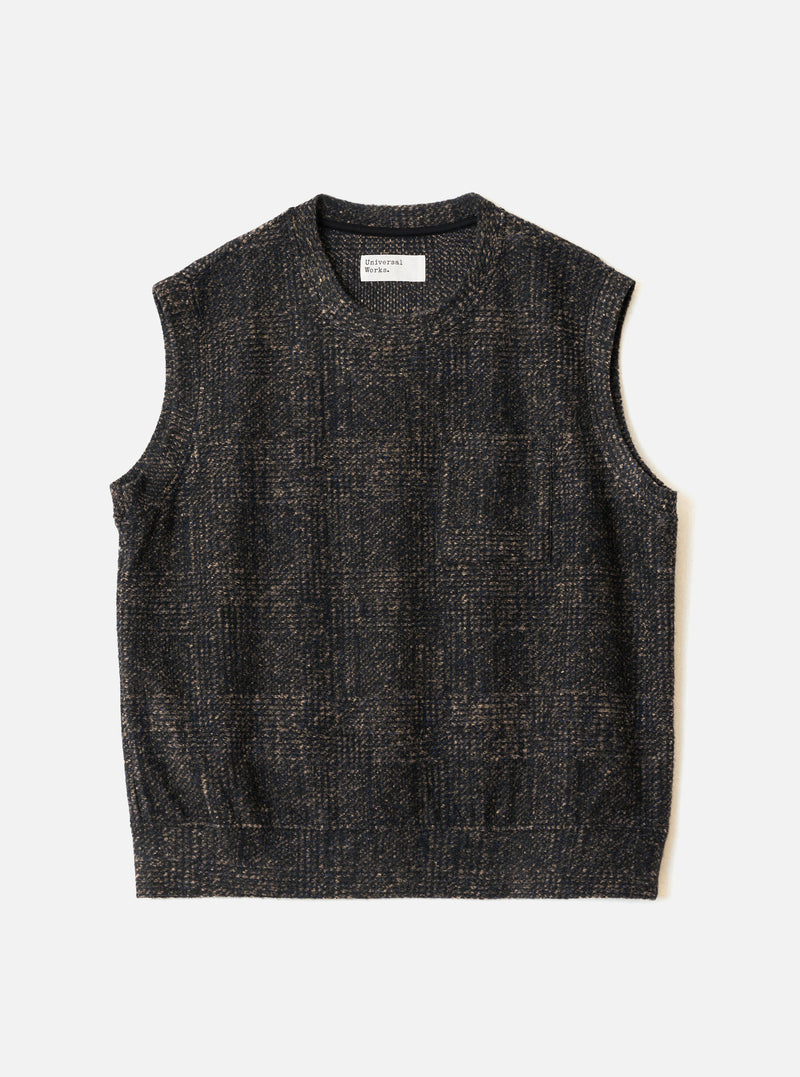 Navy sleeveless crew-neck knit vest laid flat on a light grey surface. The textured fabric features a muted check pattern in navy and tan. A Universal Works woven label sits inside the crew neck. The armholes are wide and the hem is straight and ribbed.