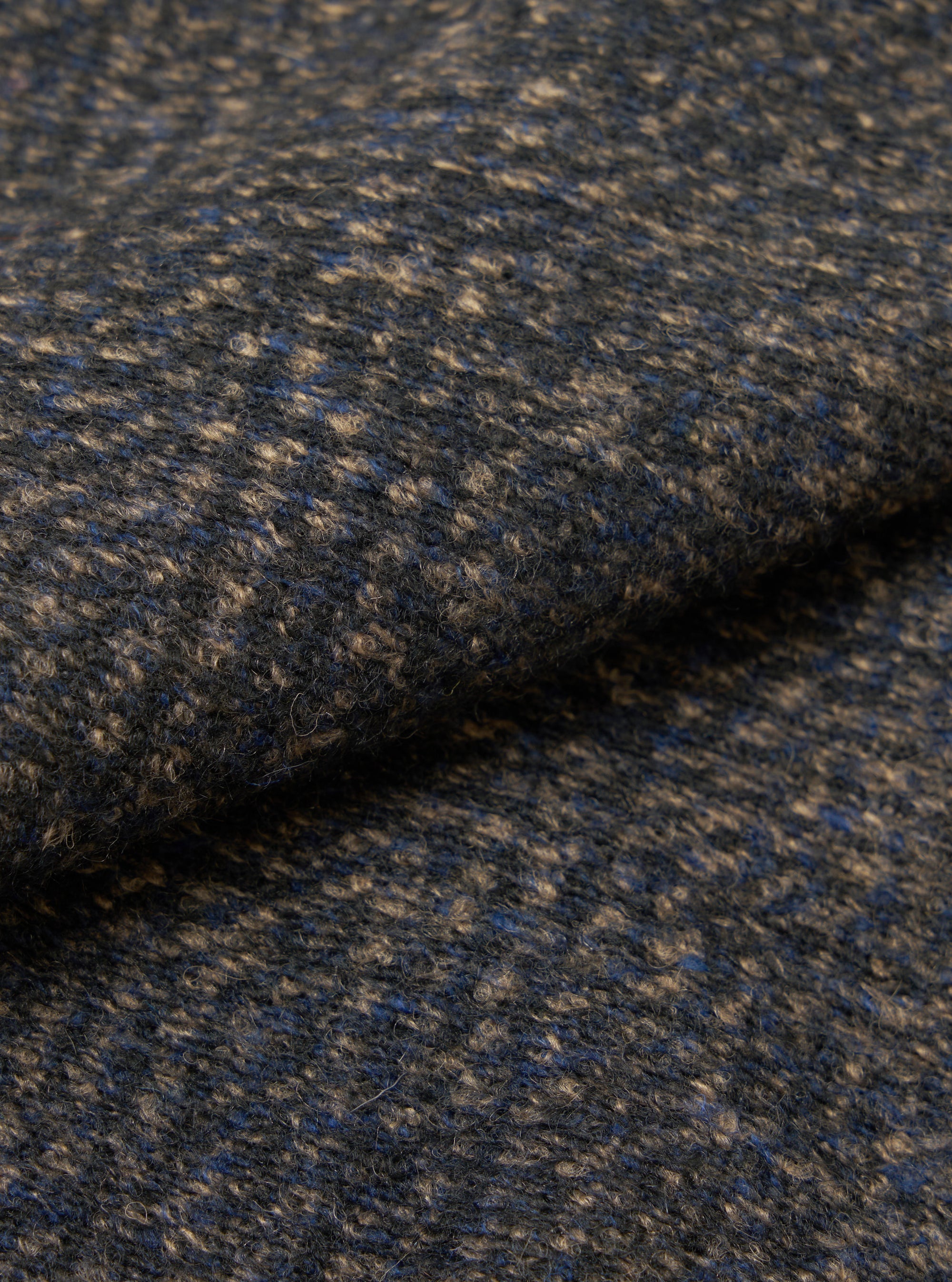 Close-up of the fabric of a navy sleeveless crew knit, showing a textured weave with flecks of camel and blue throughout. The fabric is folded, highlighting its soft, looped surface and medium weight. No background visible.