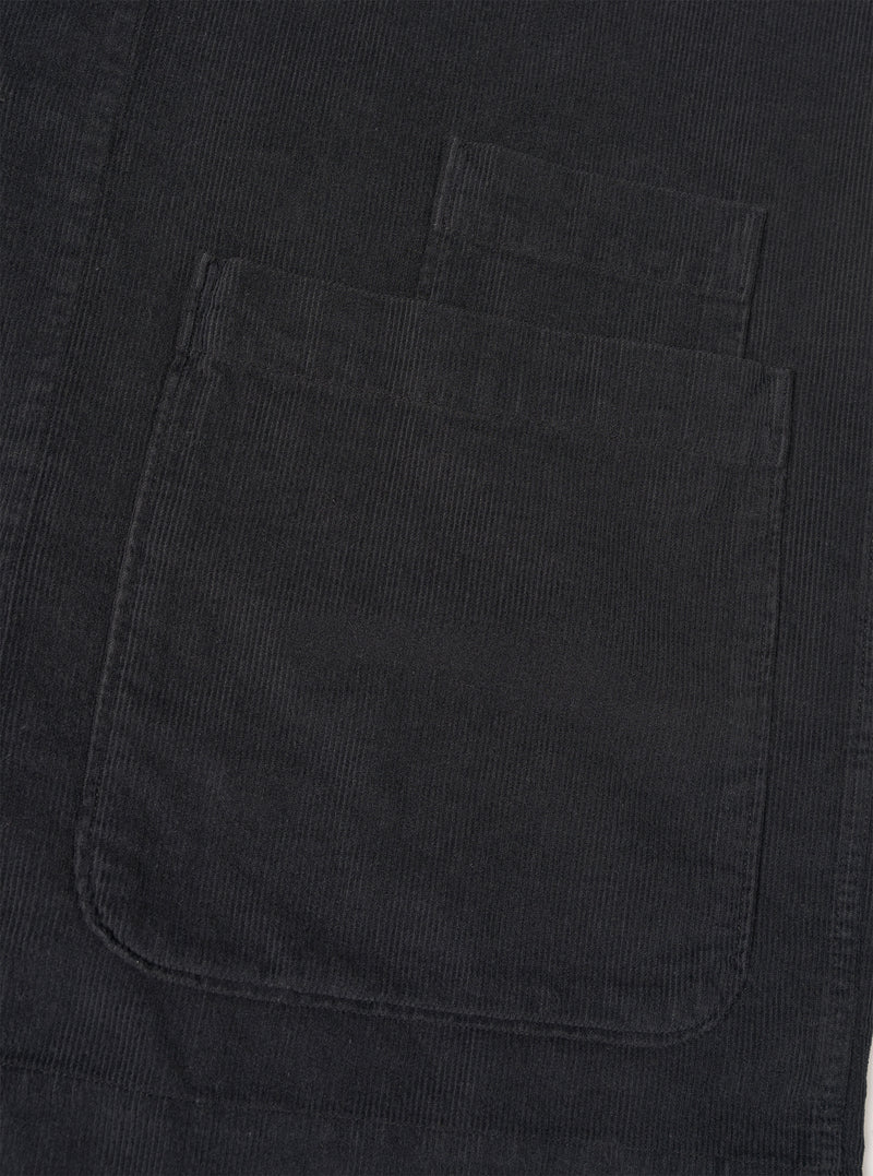 Detailed close-up shot of the Black Fine Cord Bakers Overshirt on a white background, highlighting the chest patch pocket, fine corduroy texture, button detail, and neat edge stitching on the black garment.